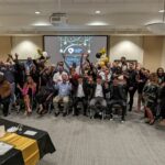 Volunteer Appreciation Ceremony attendees take a group photo, holding their hands up in the air.